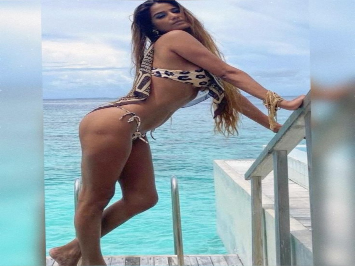 A model posing elegantly in a leopard print bikini on wooden stairs by the ocean, showcasing her confident stance.