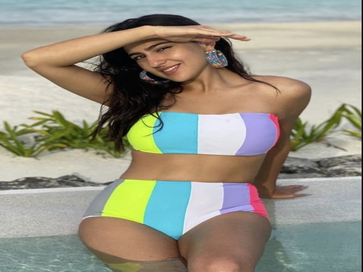 A model showcasing a vibrant striped bikini while sitting at the edge of a pool, surrounded by lush greenery.