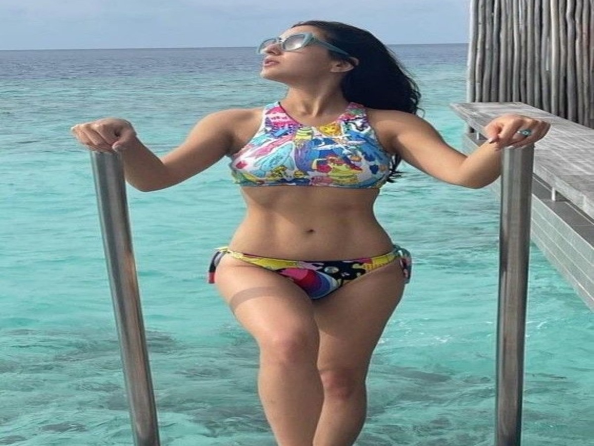 A model posing in a cartoon-themed bikini, standing by the pool railing and exuding a fun and energetic vibe.