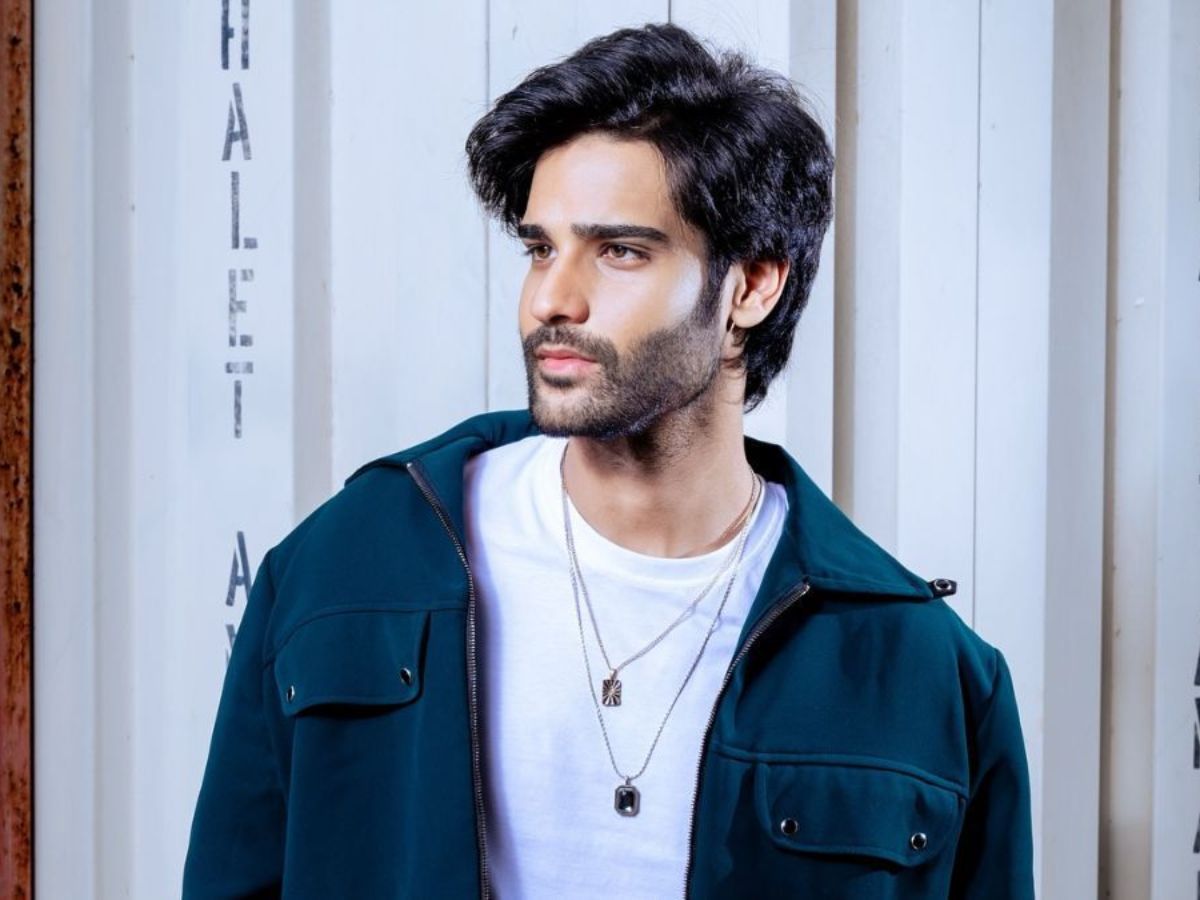 Aaman Devgan looking sideways in a teal jacket with layered chains