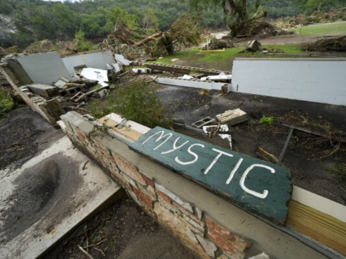 Flood-damaged Camp Mystic with broken sign and destroyed area.