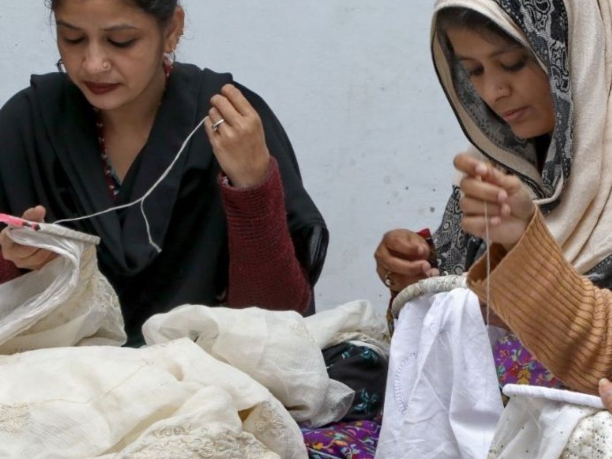 Elderly artisan stitching intricate designs on fabric by hand.
