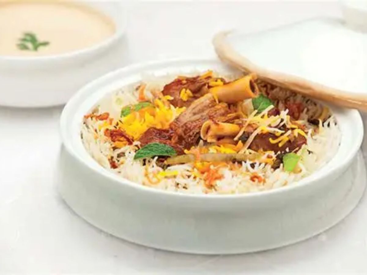 White ceramic pot filled with saffron-topped mutton biryani and herbs