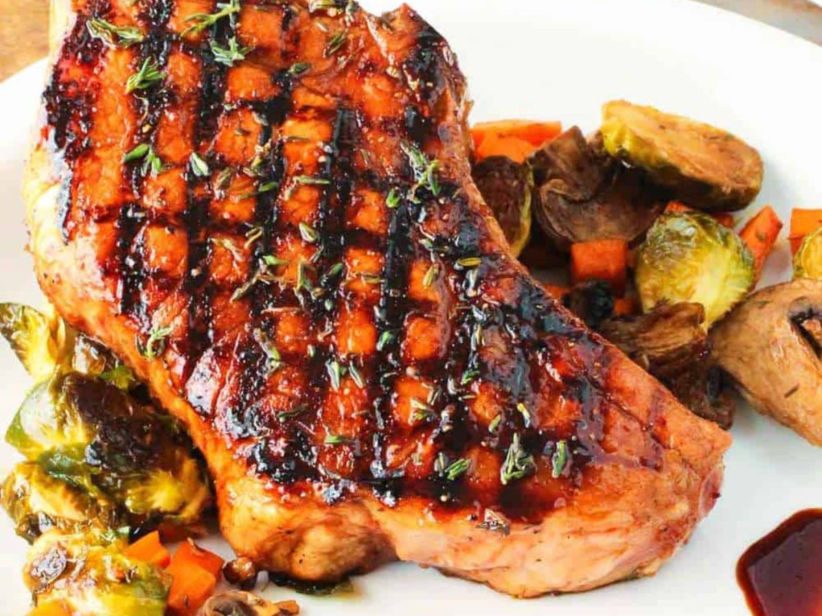 Close-up of juicy grilled pork chop with vegetables on a white plate.