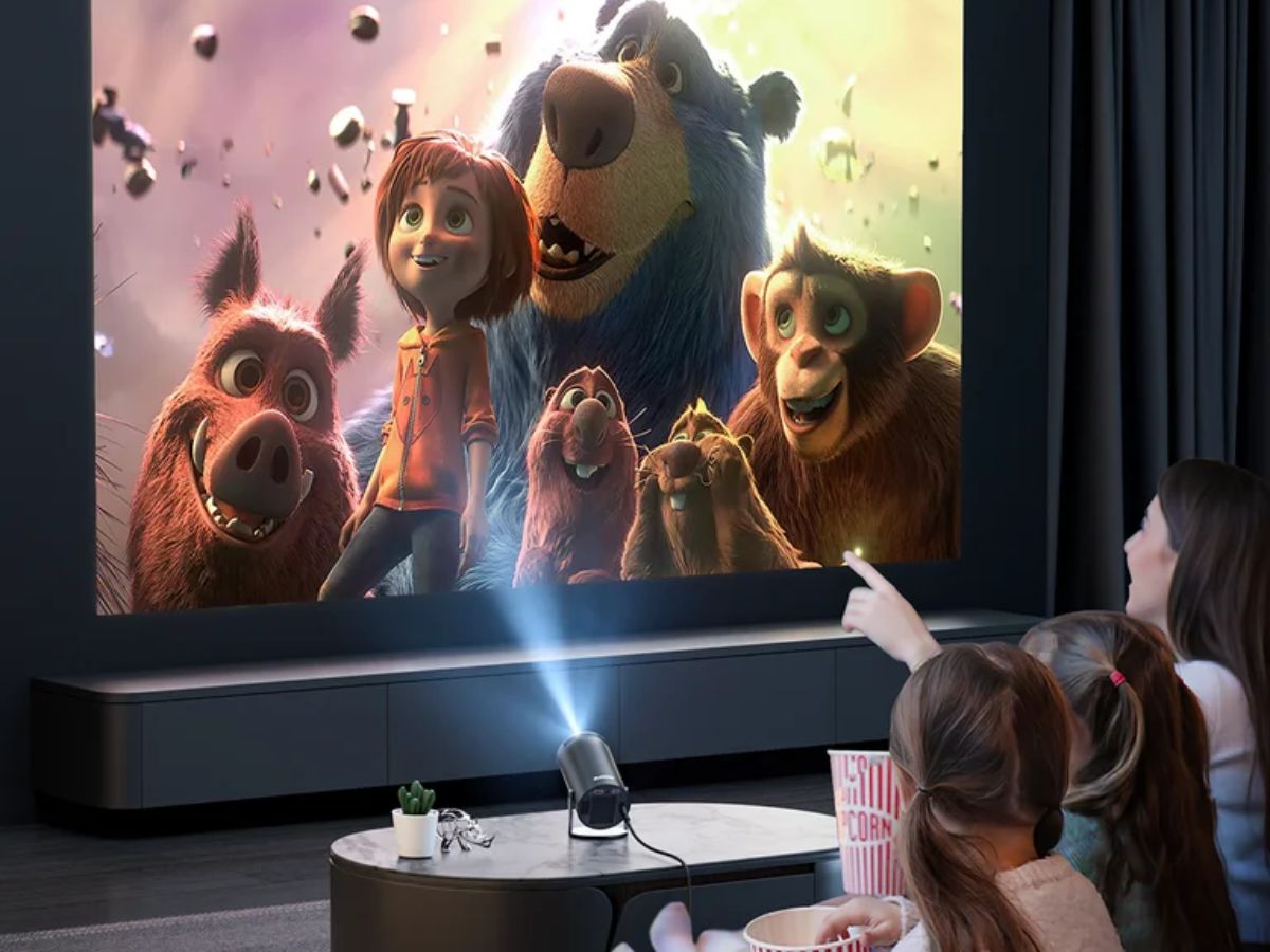 A family sits together watching a large projected animated movie on a screen in a dark living room, with a projector on a coffee table and popcorn nearby.