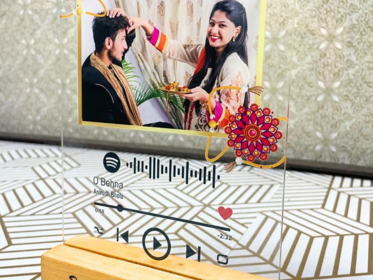 A personalized acrylic plaque with a photo of a brother and sister, a Spotify music player design, and a Rakhi motif. The plaque is a sentimental and modern gift.