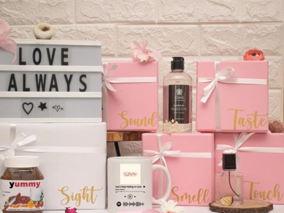 A creative gift set with five boxes representing the senses, labeled "Sound," "Taste," "Sight," "Smell," and "Touch," alongside a "LOVE ALWAYS" light box and other gift items.