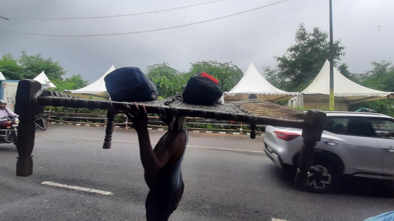 A man carrying his camping cot and other belongings.