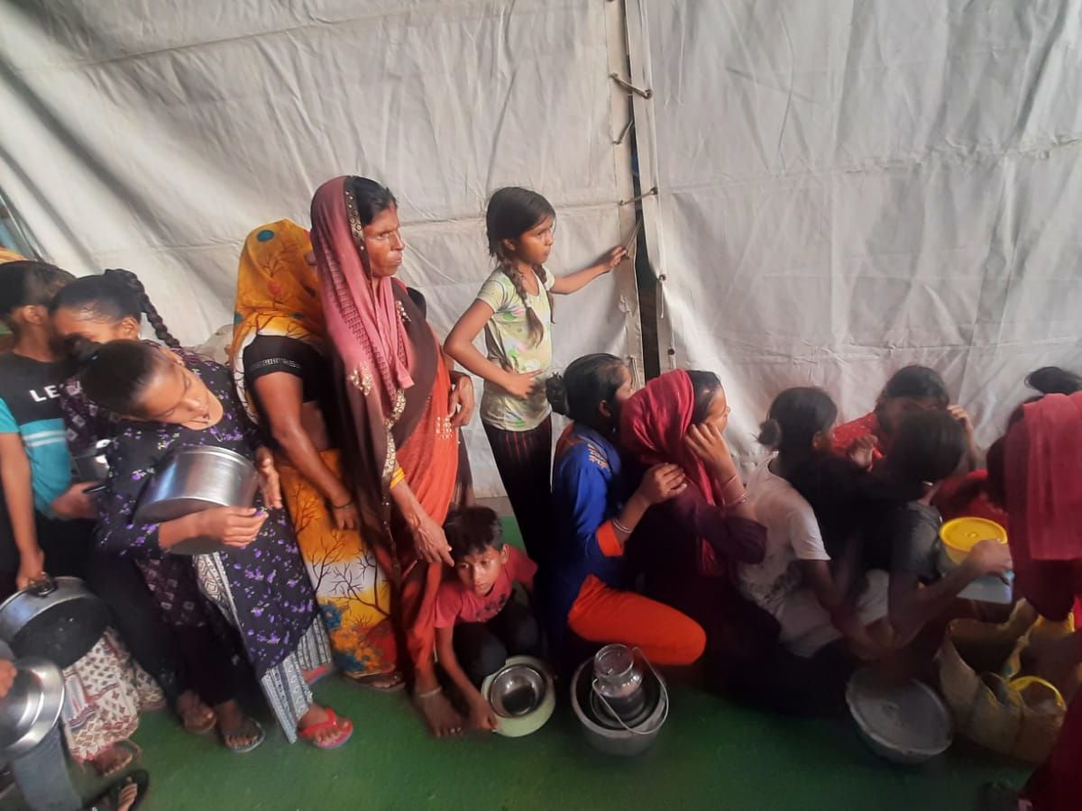 Women and children wait patiently in Delhi’s flood relief camp, hoping for their next meal.